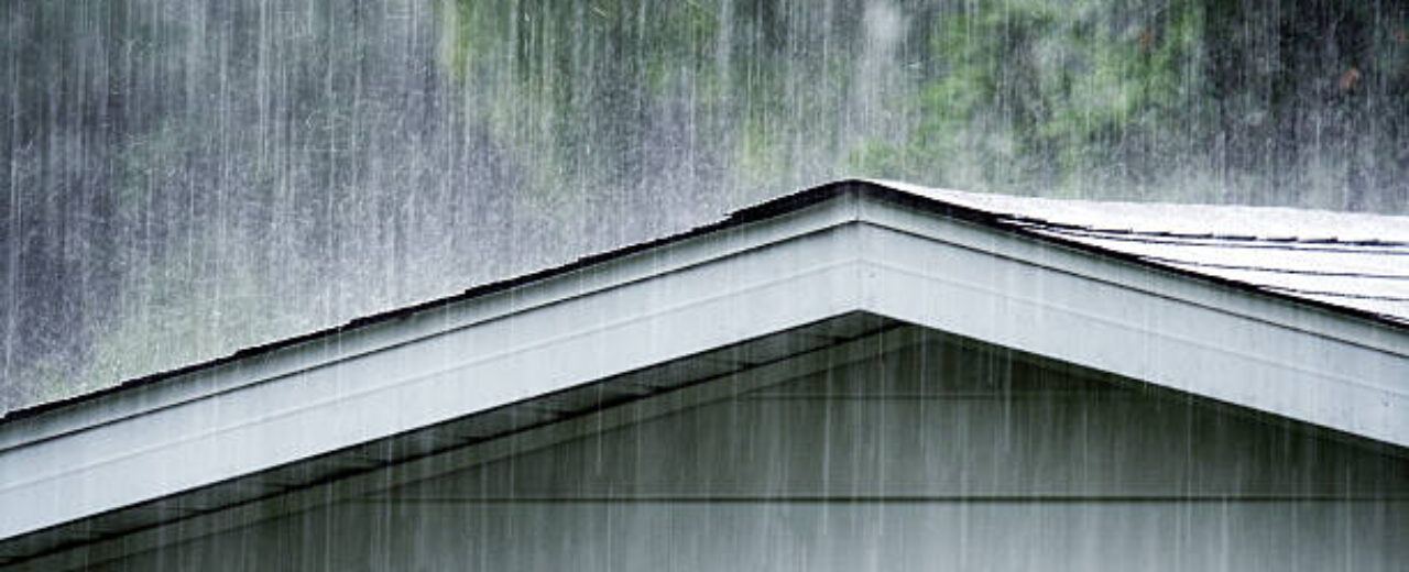 Drenching June summer rain storm downpour pounding and splattering water on a grimy old backyard clapboard siding shed roof.